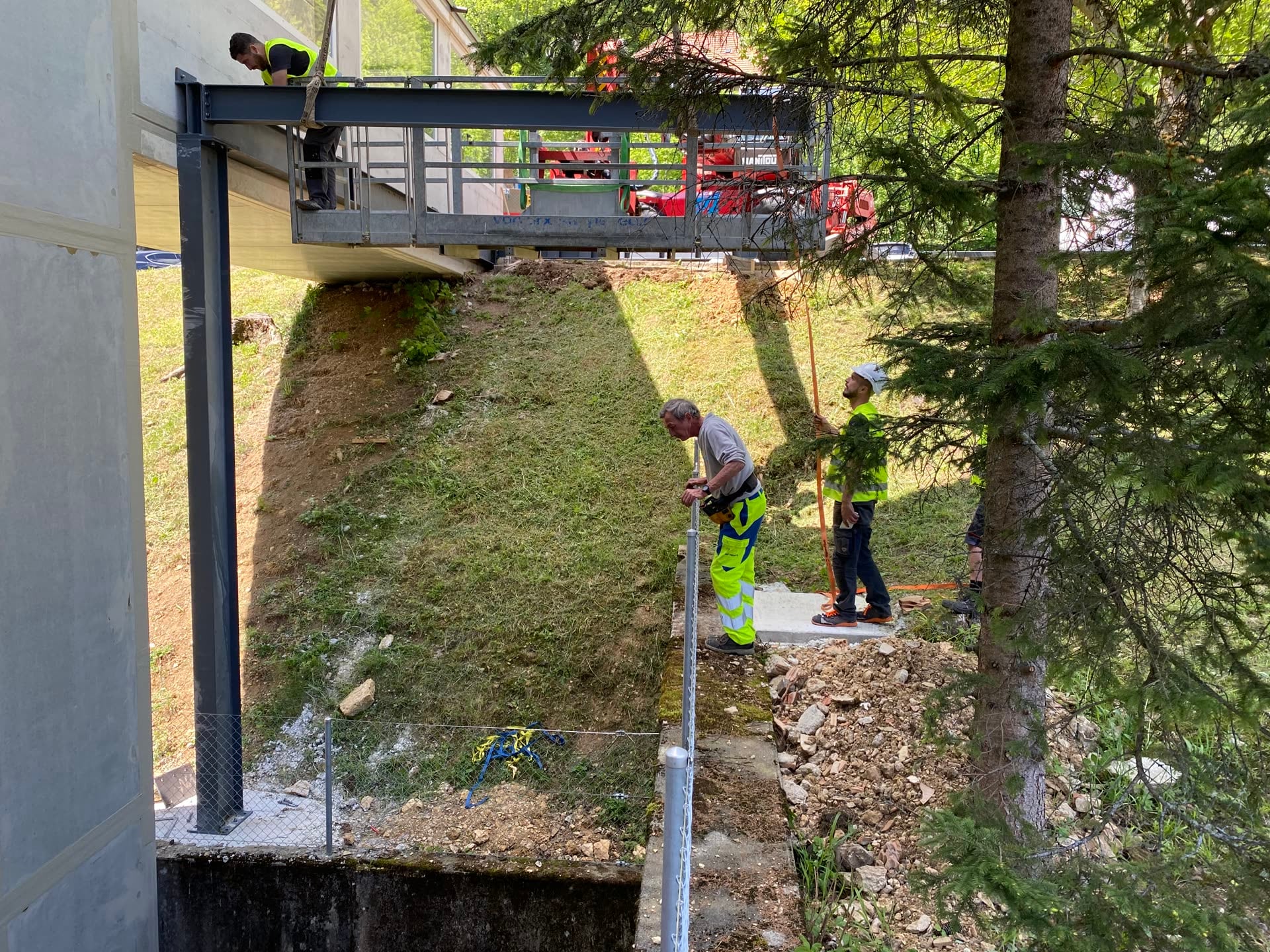 Monteurs au travail sous une passerelle métallique portée par un poteau en acier — Rue des Roches, Saint-Imier (BE)